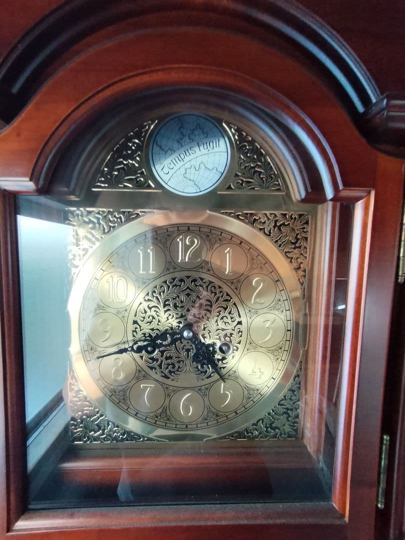 装飾的な文字盤と振り子を持つダークウッドの柱時計