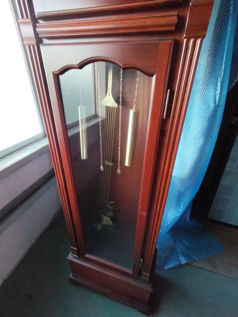 装飾的な文字盤と振り子を持つダークウッドの柱時計