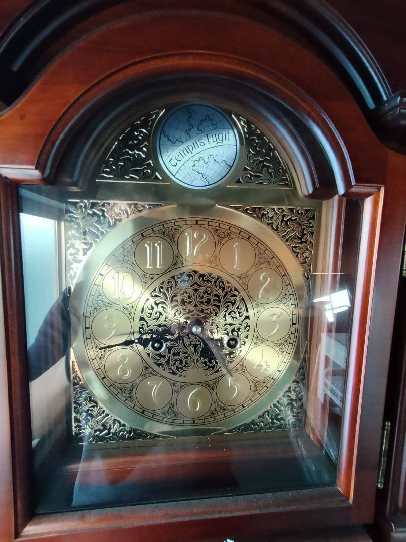 装飾的な文字盤と振り子を持つダークウッドの柱時計